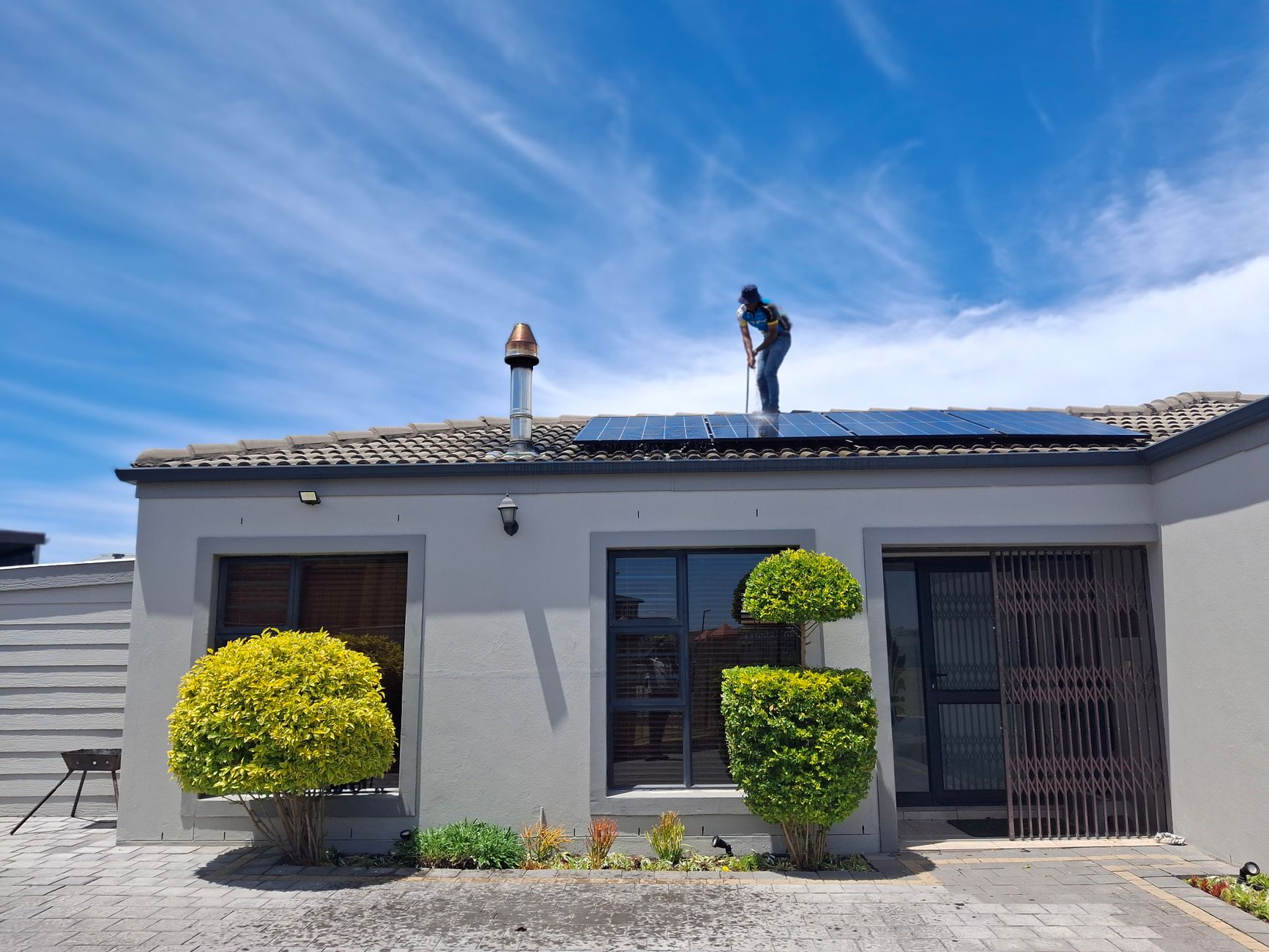 A worker installs solar panels on a house roof under a clear blue sky, showcasing renewable energy adoption.